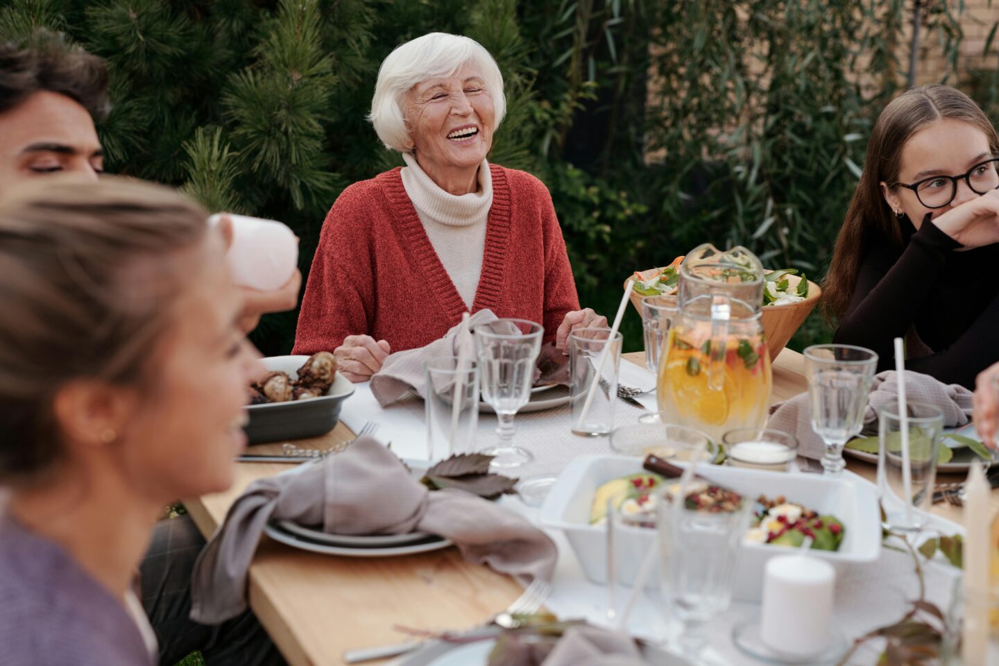 Elderly woman laughing while seated at an outdoor table surrounded by loved ones—capturing the warmth, connection, and shared joy of mindful, communal eating.