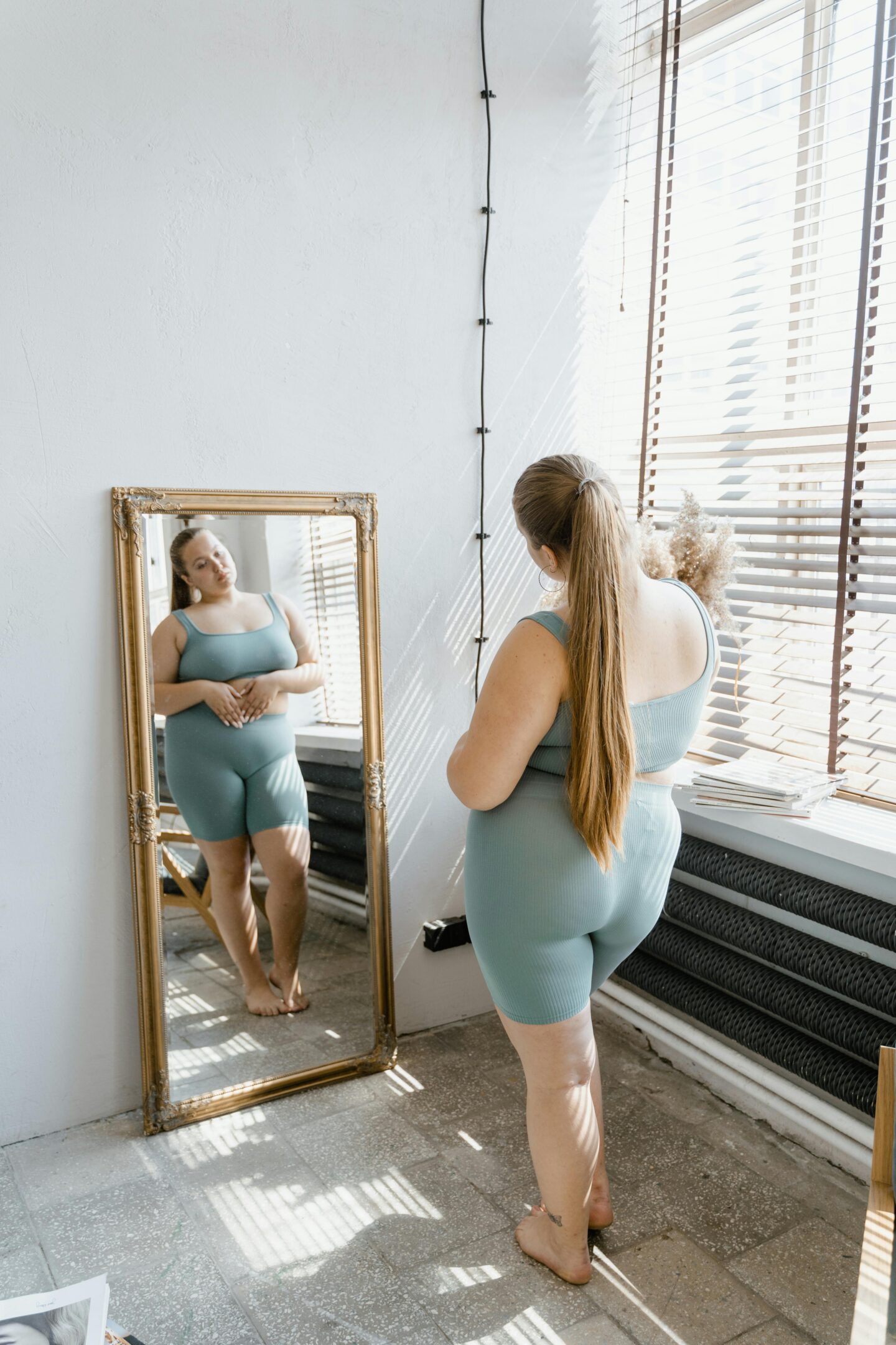 Woman in activewear standing in front of a mirror, gently observing her reflection—capturing the vulnerability and power of body image work during eating disorder recovery.