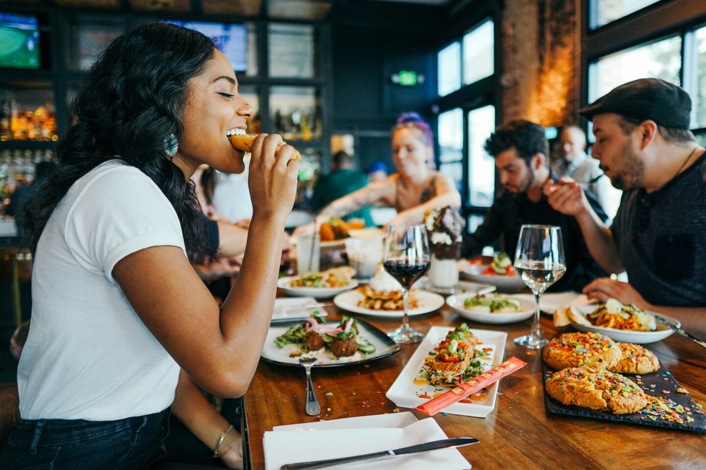 Group of people laughing and enjoying a diverse spread of food at a restaurant—highlighting social connection, food variety, and the celebration of eating in community.