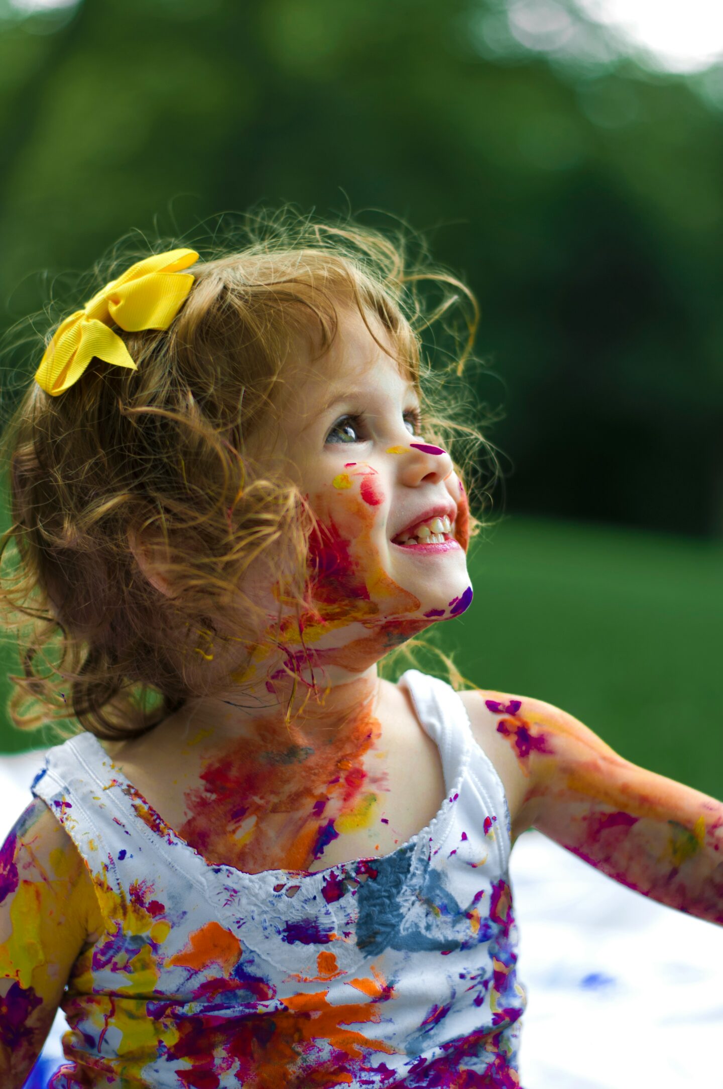 A young child joyfully covered in colorful paint, looking upward with delight—representing the inner child or ‘exiled part’ in IFS, and the playful, creative energy that reemerges when protectors begin to soften.