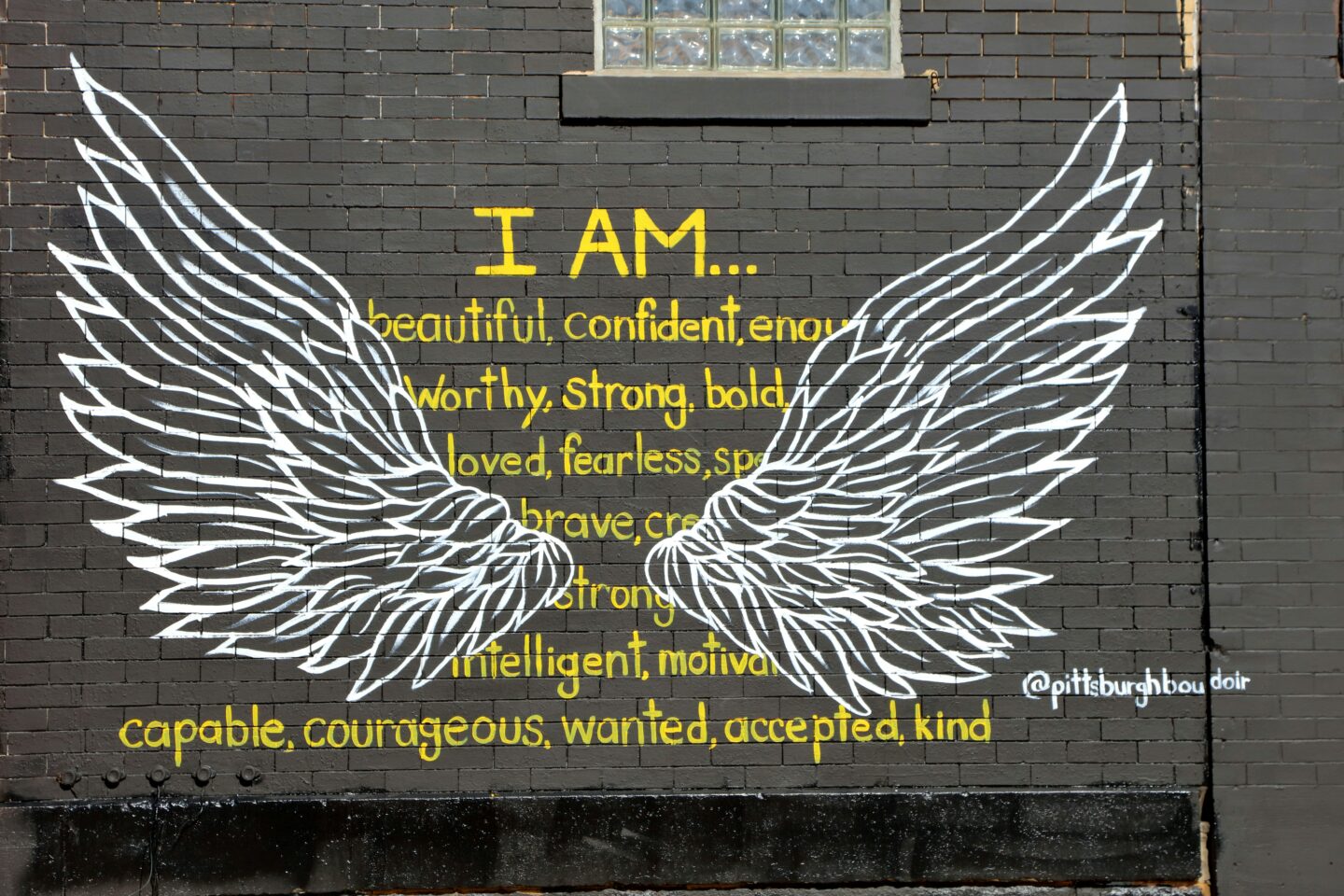 A vibrant street mural of angel wings on a brick wall, surrounded by empowering affirmations like “I am beautiful, confident, enough”—symbolizing the process of reclaiming self-worth and challenging shame-based beliefs in body image recovery.