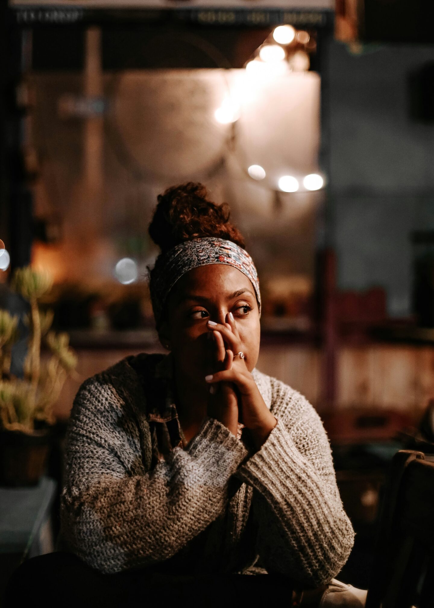 A woman sits in a cozy, dimly lit setting, resting her hands on her face in thoughtful contemplation—capturing the emotional weight of shame and the quiet strength found in moments of self-reflection during eating disorder recovery.