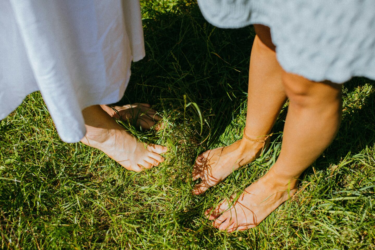 Two people standing barefoot on sunlit grass, representing grounding techniques in somatic therapy that help reconnect with the body and reduce food-related stress.