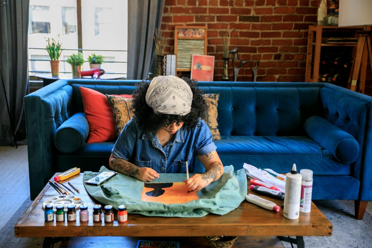 Person painting at a coffee table in a colorful, cozy living room—representing creativity, self-expression, and grounding practices that support emotional regulation and healing.