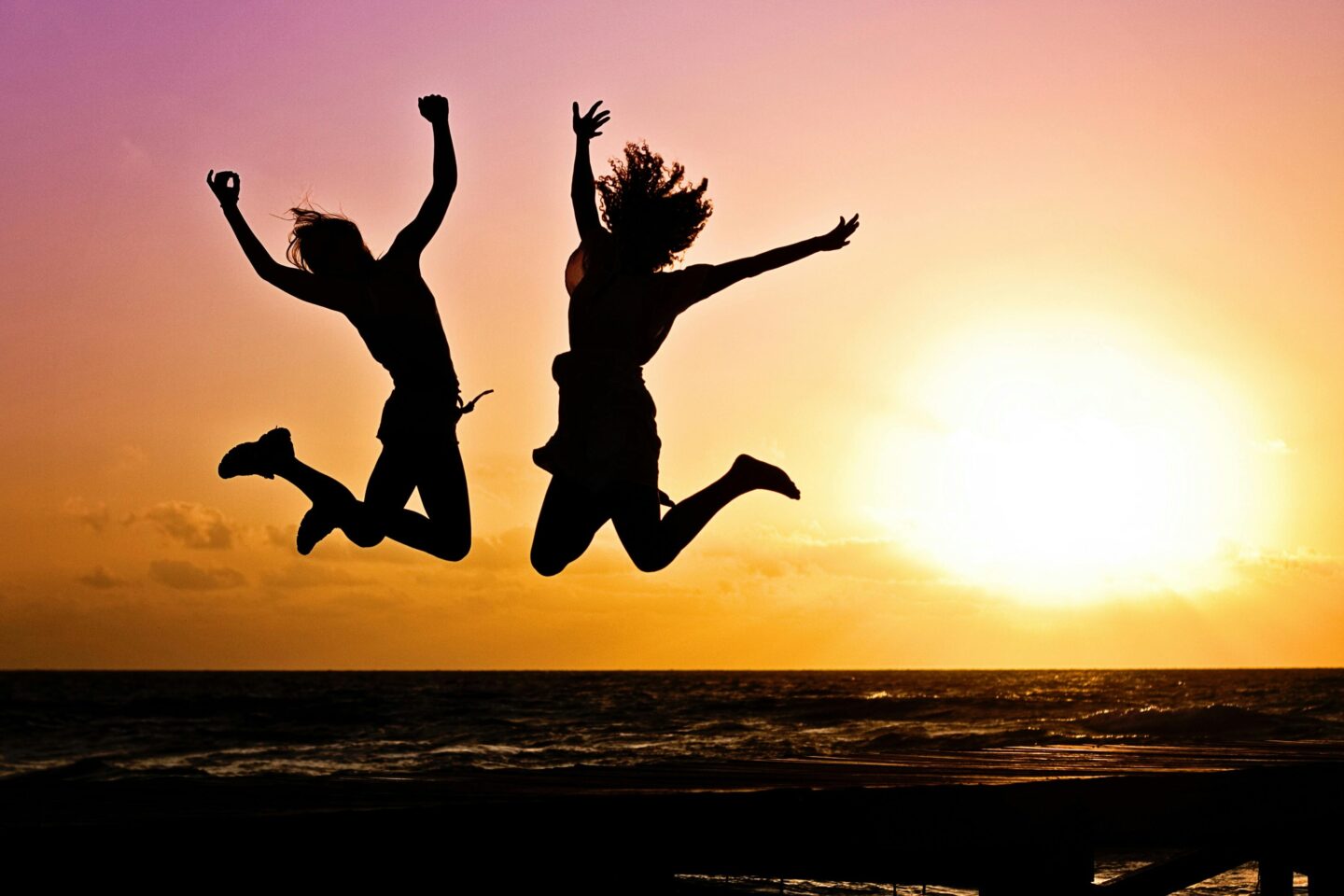 Two people jumping joyfully in front of a sunset at the beach—capturing the freedom, vitality, and emotional uplift that can come with healing and balanced energy restoration.
