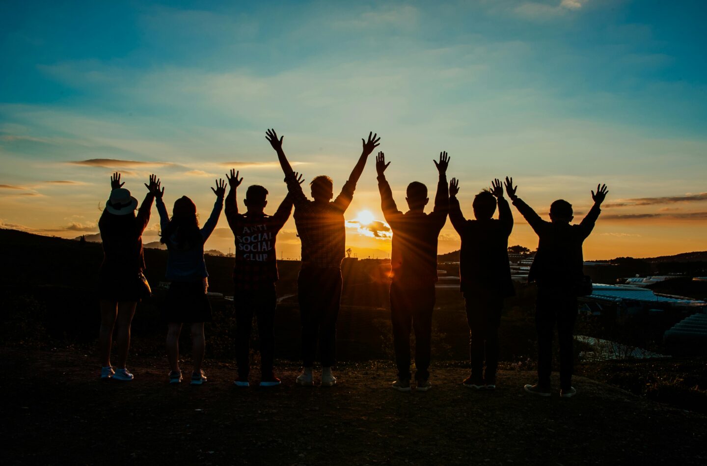 Silhouettes of people standing together with arms raised toward a sunset—symbolizing connection, freedom, and collective joy in the recovery journey.