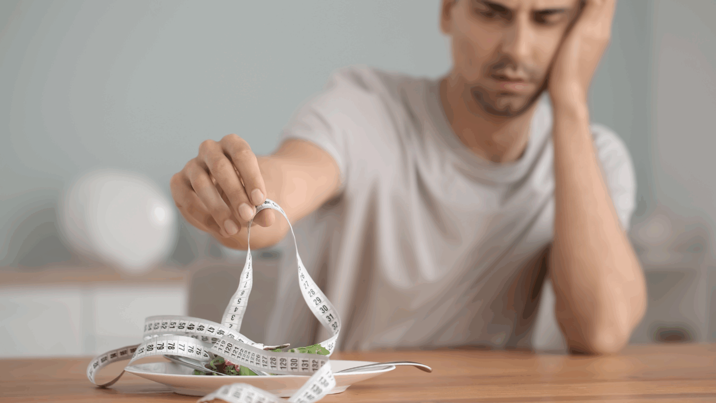 Man stares at a measuring tape and vegetables on a plate. Begin online eating disorder therapy in San Jose, California at Kindful Body.