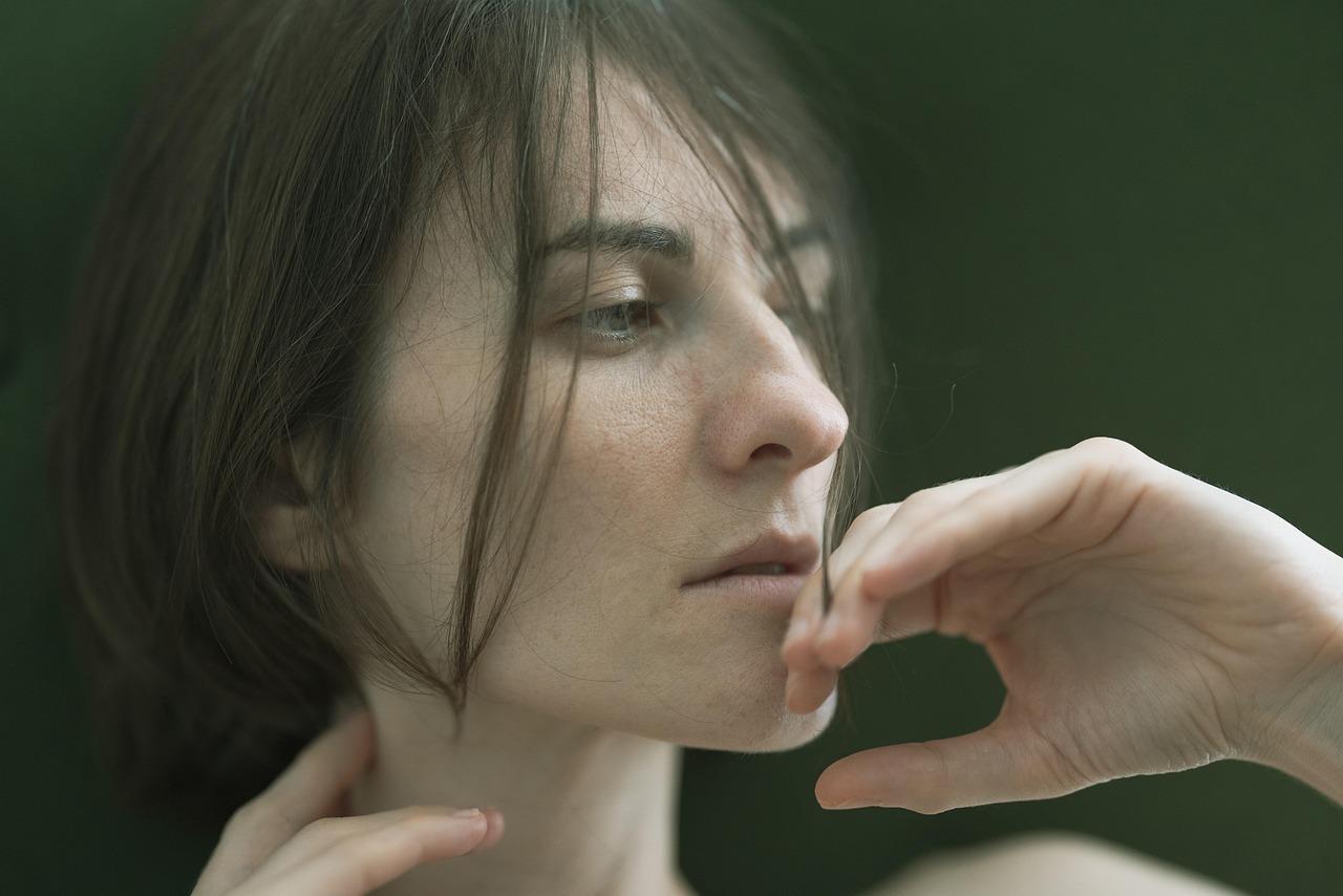 Person in side profile looking thoughtful, with their hand near their face and a soft, blurred green background.