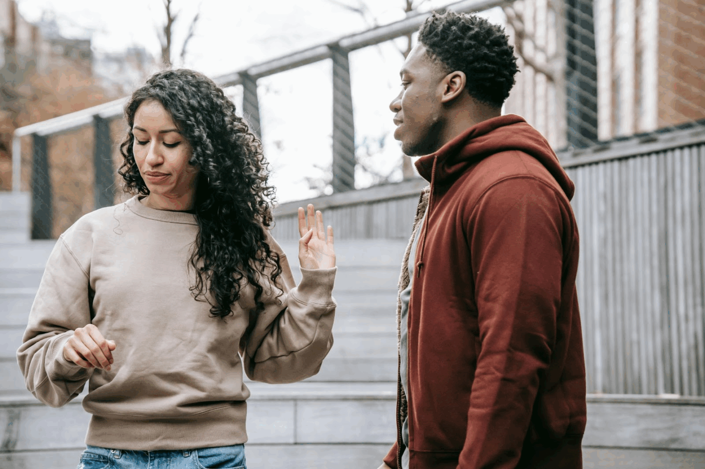 A woman raises her hand to signal discomfort or disagreement in a conversation with a man outdoors. This image illustrates the real-life challenge of setting boundaries during diet culture discussions, especially with friends or loved ones.