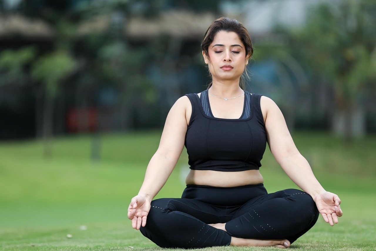 Person sitting cross-legged on grass practicing meditation, representing mindfulness tools used in CBT therapy for emotional eating and binge eating disorder recovery.